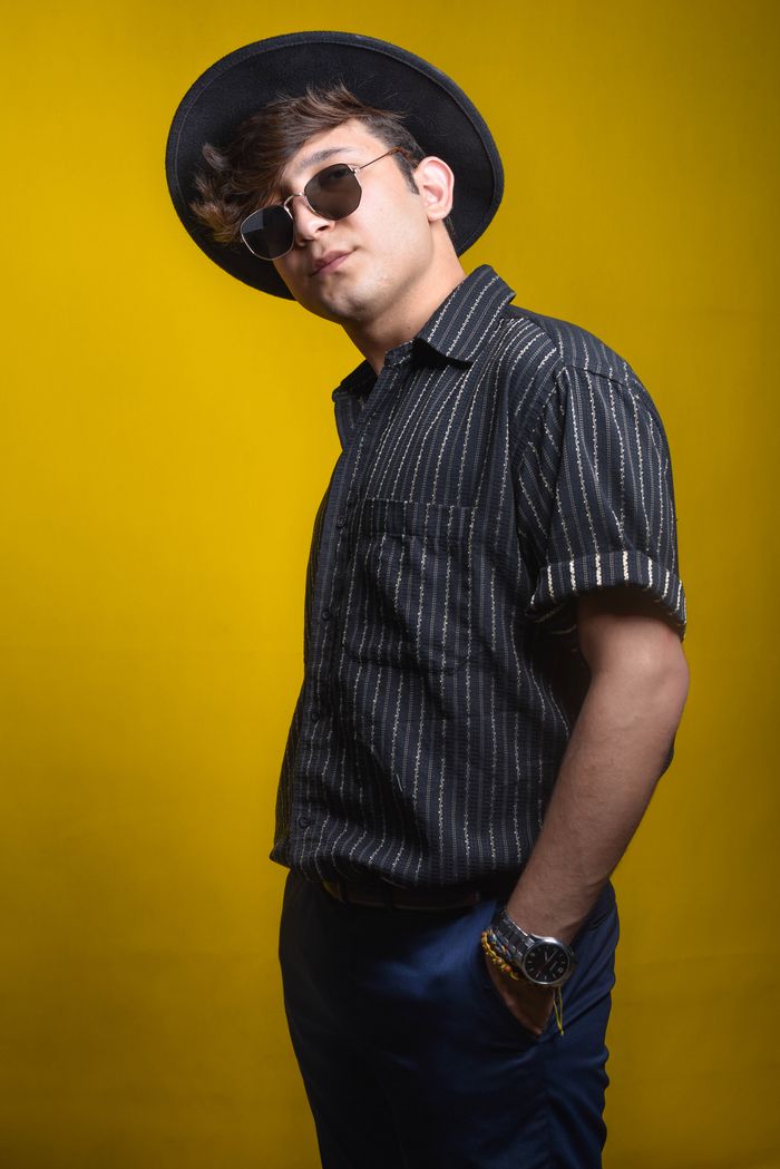 room-01 Portrait of a fashionable man wearing sunglasses and a hat against a yellow background, exuding confidence and style.