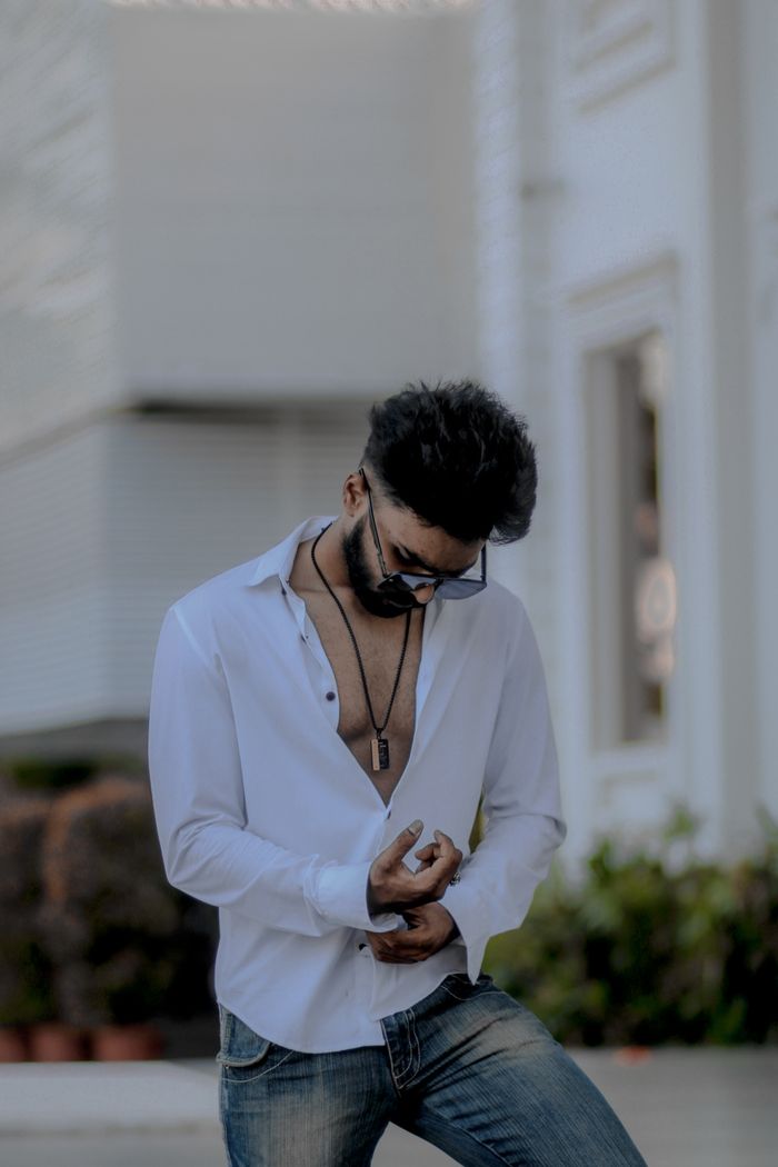 Home Casual man in sunglasses and white shirt posing confidently outside a modern building.