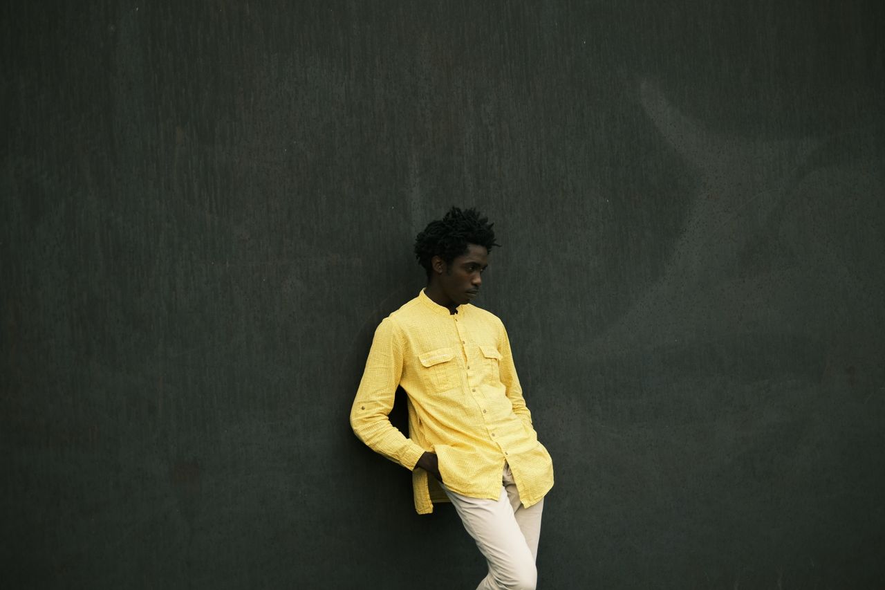 room-02 Stylish young man wearing a yellow shirt poses against a dark wall.